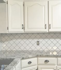 a kitchen with white cabinets and marble counter tops