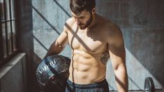 a shirtless man holding a black boxing glove and ball in his left hand while standing next to a jail cell