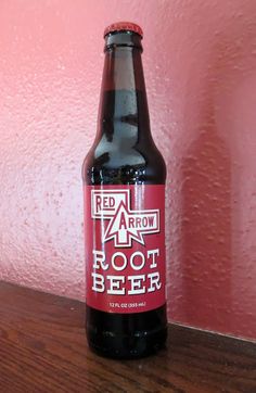 a bottle of root beer sitting on top of a wooden table next to a pink wall