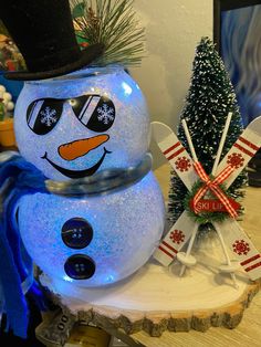 a lighted snowman sitting on top of a wooden table next to a christmas tree