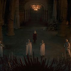 several people dressed in white are walking through a dark hall with torches hanging from the ceiling