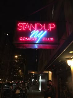 a neon sign that reads stand up comedy club on the side of a building at night