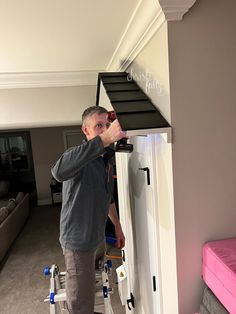 a man standing next to a ladder in a living room with pink couches and white walls