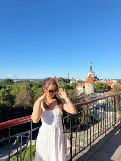 a woman standing on top of a balcony next to a metal railing with trees in the background