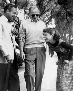 three people standing next to each other in front of trees and one person is laughing