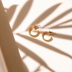 a pair of gold hoop earrings sitting on top of a white table with shadow from the wall