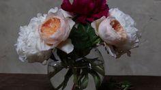 a vase filled with white and red flowers on top of a wooden table next to a wall