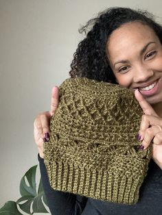 a woman is smiling while holding up a knitted purse with her finger on it