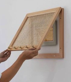 a person holding up a wooden frame with holes in it to see if something is on the wall