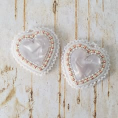 two white heart shaped brooches with pearls and beading on wooden background, top view