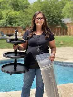 a woman standing next to a pool holding a water bottle and tray with drinks on it