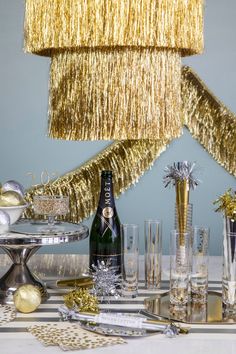 A table with a champagne bottle and glasses, adorned with Meri Meri's Gold Tinsel Chandelier. Tinsel Chandelier, Holiday Event Decor, Fringe Garland, Handmade Halloween Decorations, Christmas Party Themes, Gold Party Decorations, Gold Birthday Party, Tinsel Garland, Nye Party