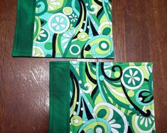 two placemats with green and blue designs on them sitting on a wooden table