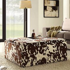 a cow print ottoman sitting on top of a white rug in front of a window