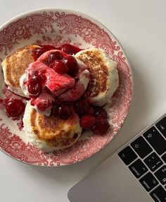 a plate topped with pancakes covered in fruit next to a laptop computer on a table