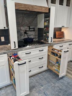 an open cabinet in a kitchen with white cabinets and marble counter tops on the island