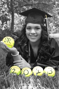 a woman in graduation cap and gown laying on the grass with softballs that say 2012