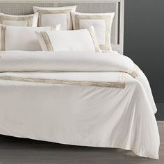 a bed with white linens and gold trimmings on the headboard is shown