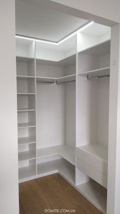 an empty walk in closet with white shelving and wooden flooring on the side