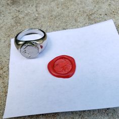 a red wax stamp sitting on top of a piece of paper next to a silver ring