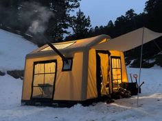 a tent is set up in the snow with its door open and lights on at night