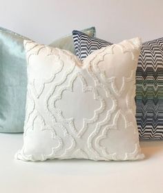 three decorative pillows are lined up on a white surface, one is blue and the other is green