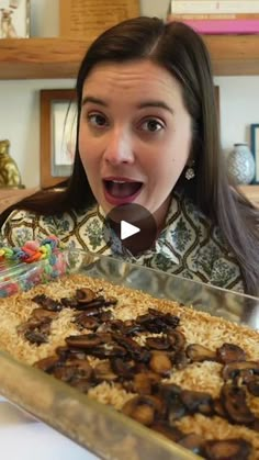 a woman making a surprised face in front of a pan filled with mushrooms and rice