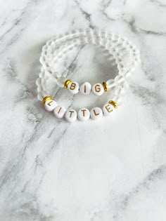 two white and gold bracelets with the word big brother written on them, sitting on a marble surface