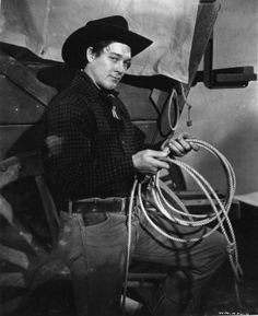 black and white photograph of a man in cowboy attire holding a rope with his hands