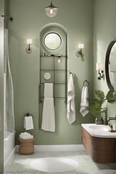 a bathroom with green walls and white towels hanging on the wall, along with a round window