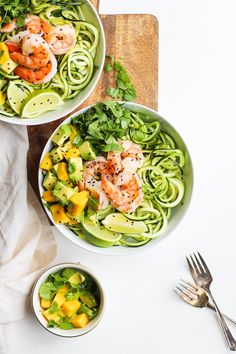 two bowls filled with pasta and shrimp on top of a wooden cutting board next to silverware