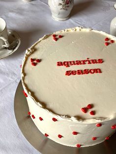 a white cake with red hearts on it sitting on a table next to cups and saucers