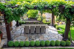 an outdoor dining table and chairs surrounded by greenery in a garden area with stone walkway