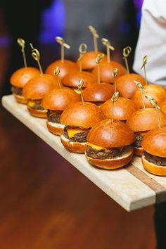 several mini hamburgers are arranged on a wooden tray with toothpicks in the middle