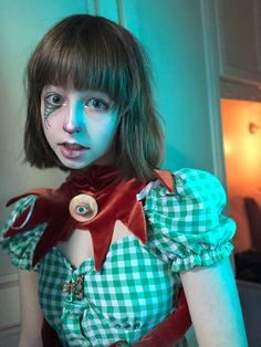 a woman with makeup painted on her face and neck, wearing a green checkered dress