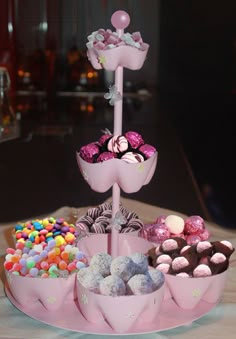 there is a pink cake stand with lots of candies on it and chocolates in the middle