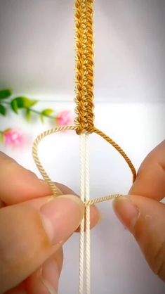 two hands are holding a piece of gold string with a heart shaped knot on it