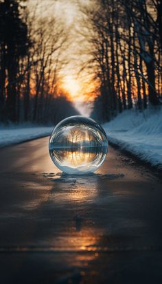 a glass ball sitting on the side of a road in the middle of snow covered ground