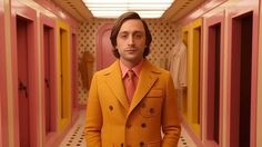 a man in an orange suit and pink tie standing in a hallway with yellow doors