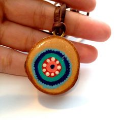 a hand holding a wooden pendant with an orange and blue flower on it's center