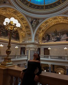 Girl wearing black dress standing in national museum of prague, her head is tilted back, she wears cherry red lipstick, she has long red nails and she’s wearing gold accessories