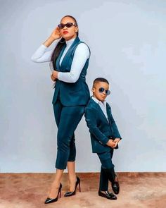 a woman standing next to a little boy in a suit and tie with sunglasses on