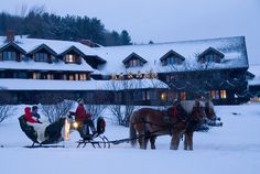 two horses pulling a sleigh in front of a large house with christmas lights on it