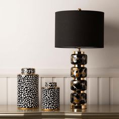 three black and gold canisters sitting on top of a table next to a lamp