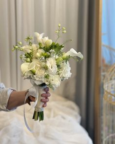 a bouquet of white flowers being held by a woman's hand in front of a bed