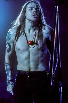 a shirtless man with long hair and tattoos holding a microphone in front of him