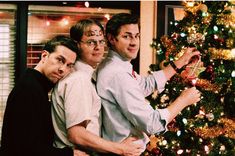 three men standing next to each other in front of a christmas tree