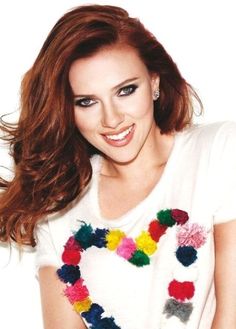 a woman with long red hair wearing a white shirt and colorful pom poms