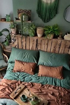 a bed covered in green and brown pillows next to a wooden headboard with potted plants on it