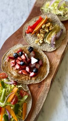 three tortillas with fruit and vegetables on a cutting board next to a salad